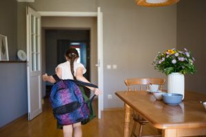 Elementary-aged girl taking off backpack while walking into the house after school.