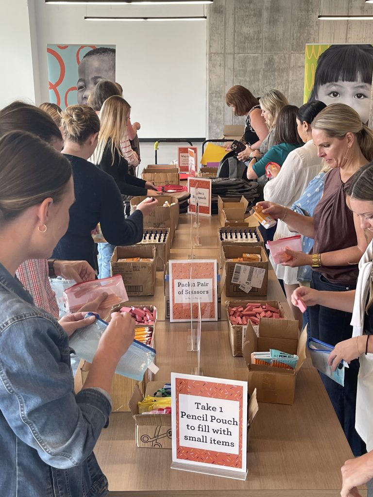 Volunteers packing backpacks at tables filled with school supplies.