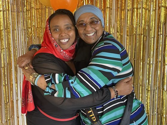 A Family Educator hugs Shany in front of a shimmery gold backdrop.