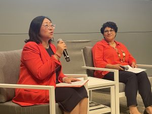 Coco Du, CEO and Melissa Meyer, VP of Development, sit in chairs on stage with microphones. Coco is speaking.