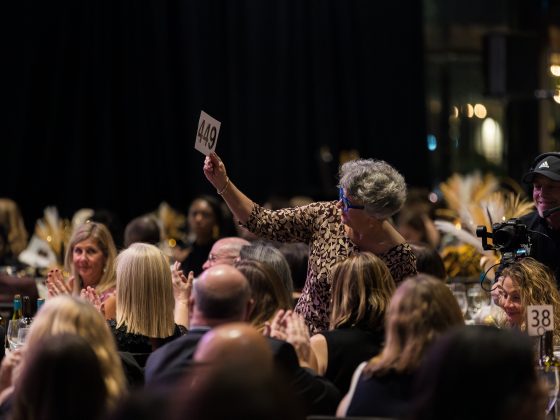 Woman holding up an auction paddle at a crowded dinner table.