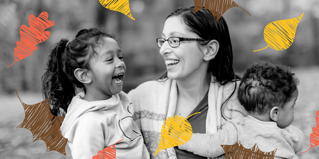 Black and white photo of a woman holding two mixed-race kids with yellow, brown, and orange illustrated leaves falling around them.