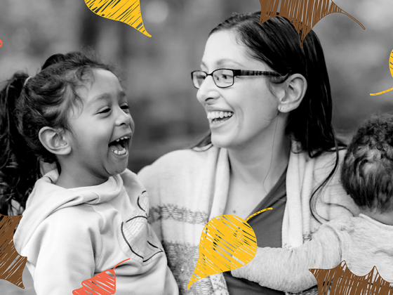 Black and white photo of a woman holding two mixed-race kids with yellow, brown, and orange illustrated leaves falling around them.