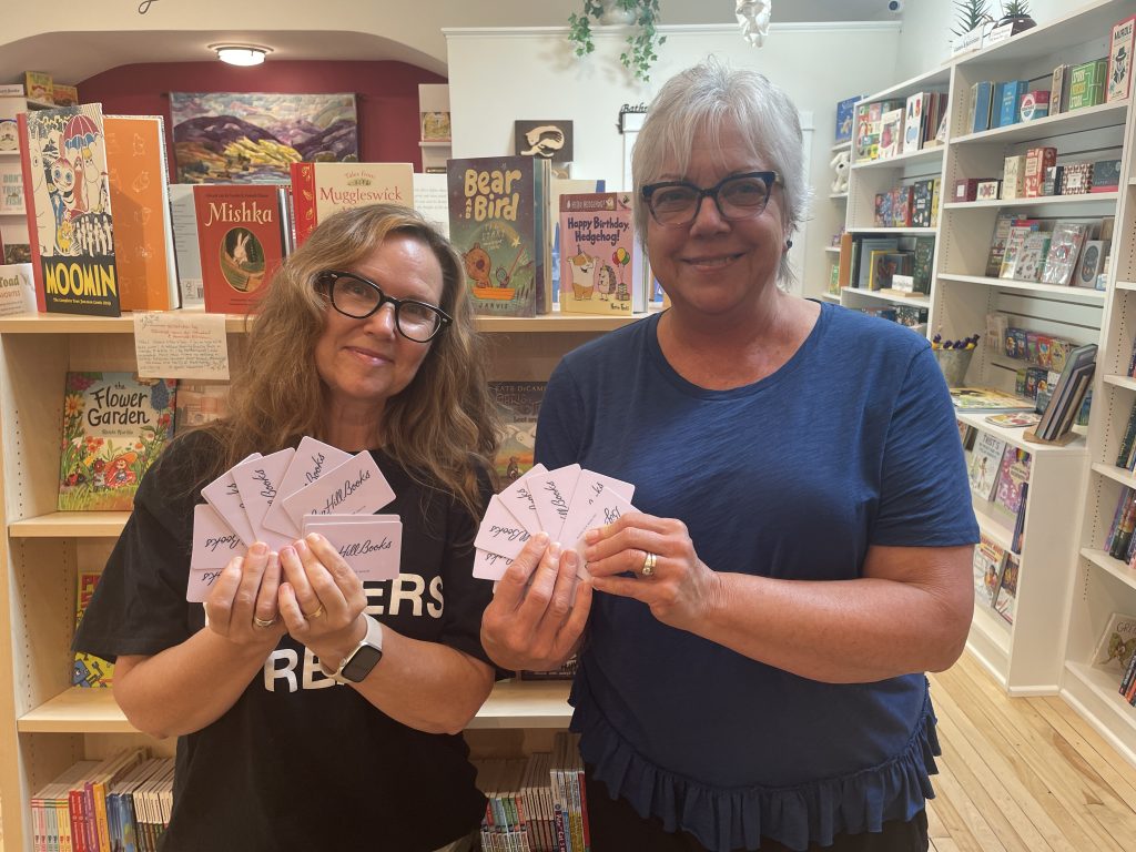 Two women holding gift cards in a bookstore.