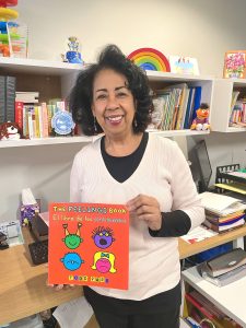 Smiling Latina woman holding a children's book titled, "The Feelings Book" by Todd Parr
