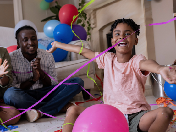 African American family celebrating in their living room with streamers and balloons.