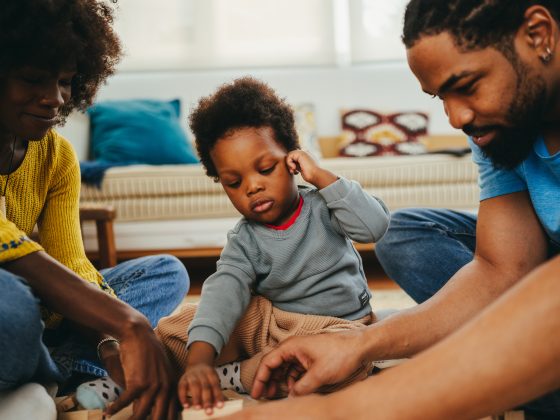 African American mother and father playing on the floor with toddler.