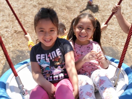 Two preschool girls swinging on a swing at the park.