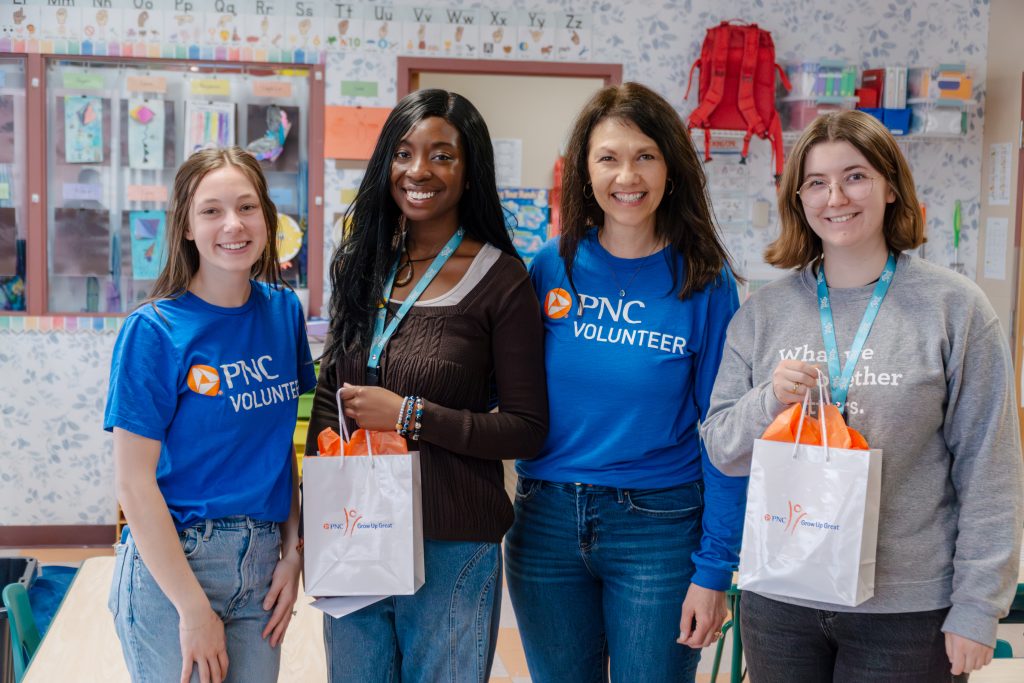 Two PNC volunteers and two Preschool Pals teachers, smiling and holding gifts from PNC.