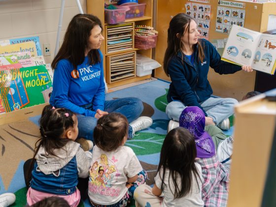 Two PNC volunteers read a story to a group of preschoolers sitting together on the floor.