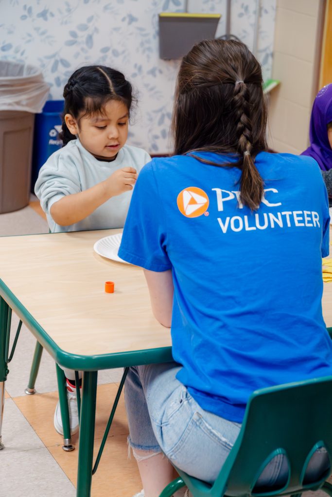 PNC volunteer helps preschooler with craft at a table.
