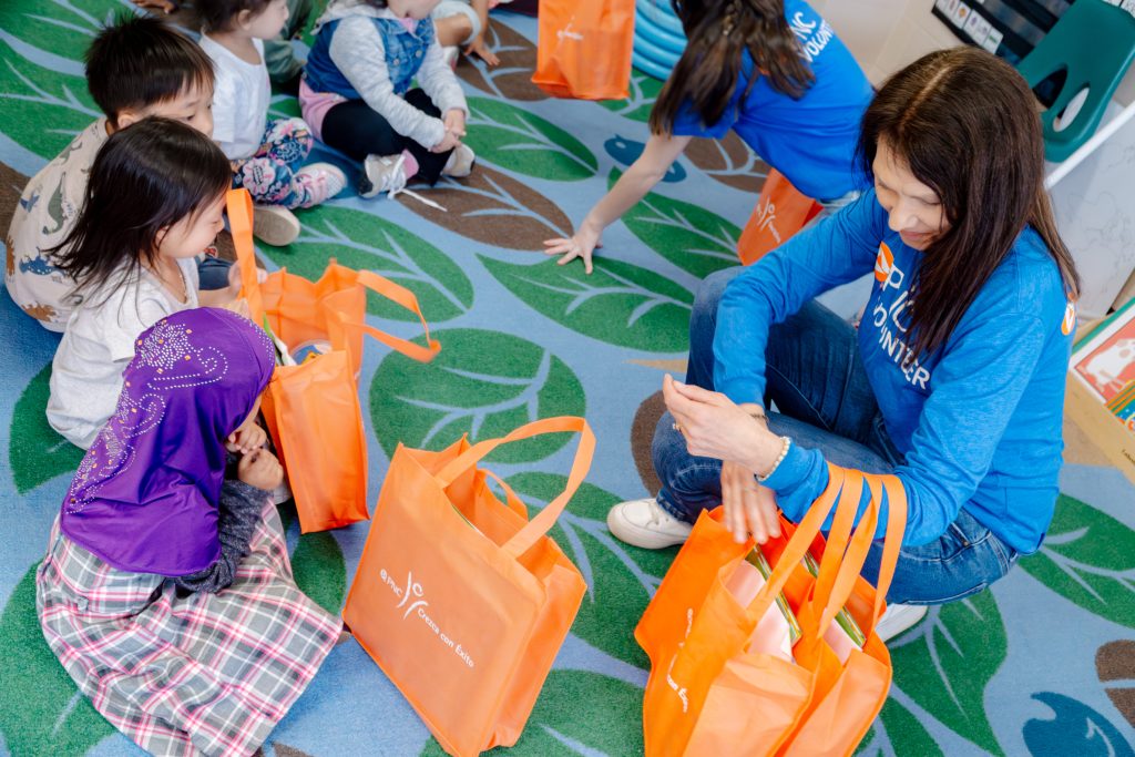 PNC volunteers pass out activity bags to students sitting in circle on the floor.