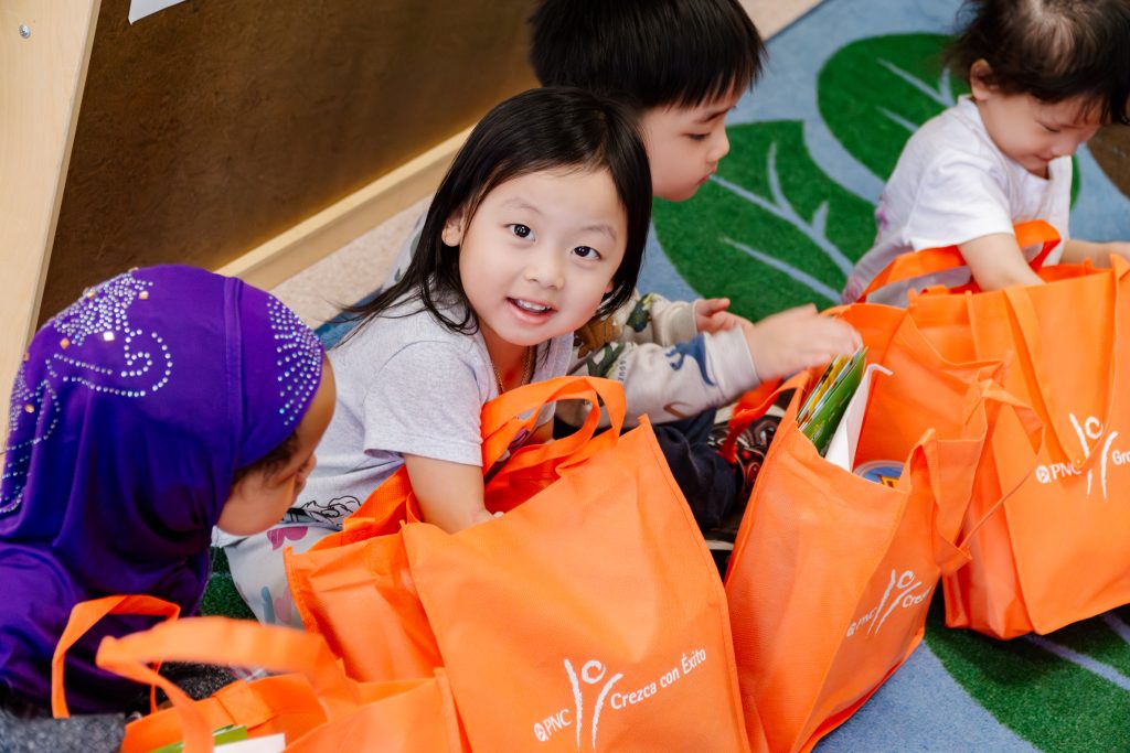 Preschoolers open orange activity bags on the floor.