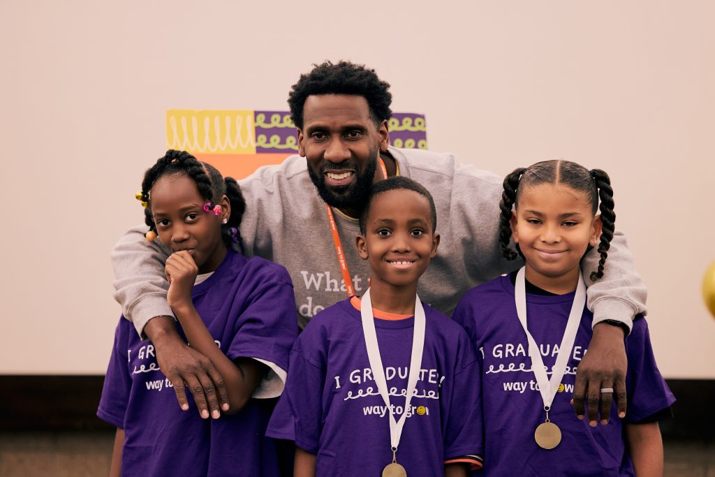 Three third graders in purple shirts and medals with a Family Educator, all smiling.