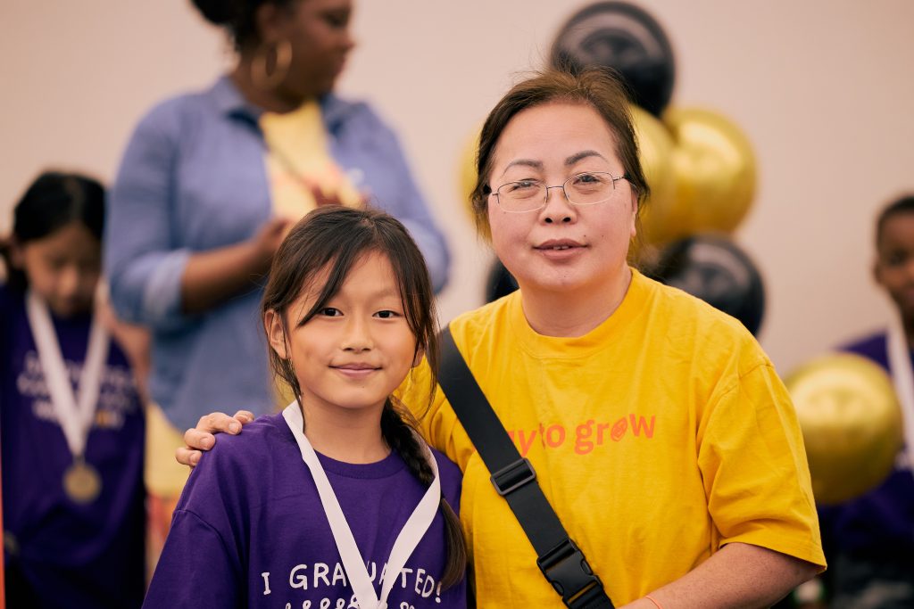 Third grader in purple shirt and medal, smiling with a Family Educator.